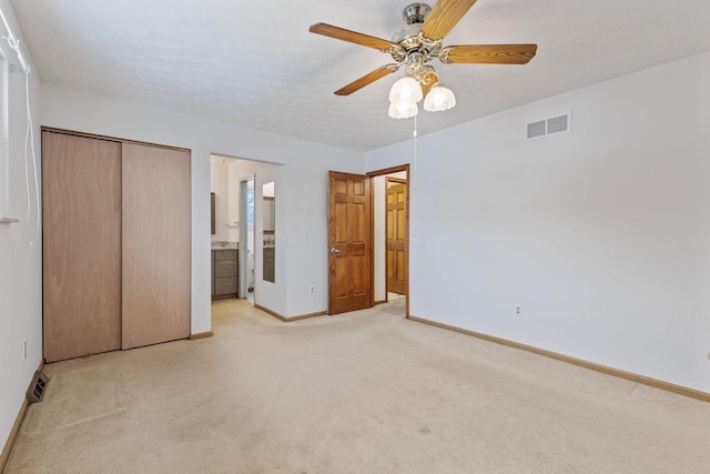 unfurnished bedroom with ensuite bath, a closet, ceiling fan, and light colored carpet