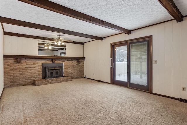 unfurnished living room featuring beamed ceiling, ceiling fan, a wood stove, carpet flooring, and a textured ceiling