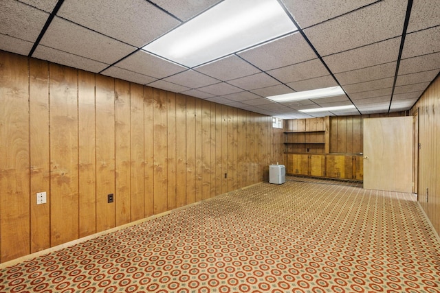 basement featuring wood walls and a drop ceiling