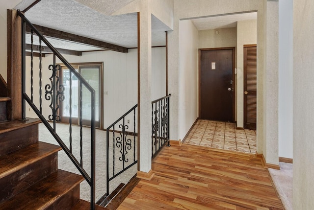 stairway with a textured ceiling, hardwood / wood-style flooring, and beamed ceiling