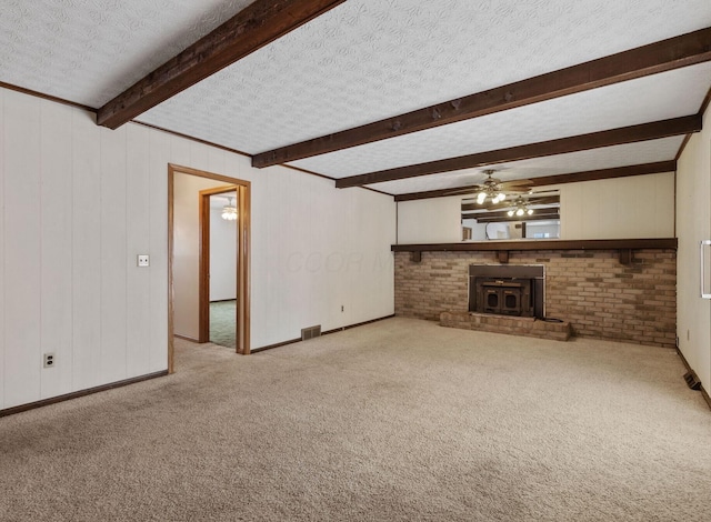 unfurnished living room with light colored carpet, beamed ceiling, ceiling fan, a wood stove, and a textured ceiling