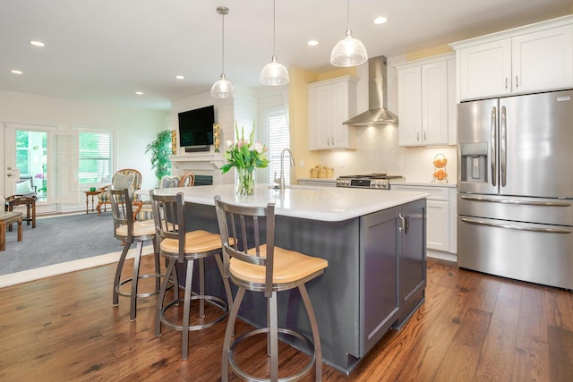 kitchen featuring white cabinetry, a kitchen island with sink, stainless steel refrigerator with ice dispenser, sink, and wall chimney exhaust hood