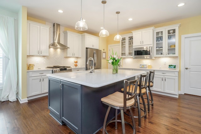 kitchen featuring hanging light fixtures, white cabinets, wall chimney exhaust hood, and stainless steel appliances