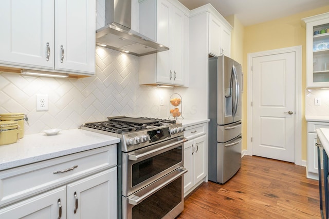 kitchen with light stone counters, white cabinets, wall chimney range hood, and appliances with stainless steel finishes