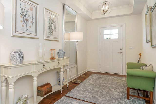 entryway with a tray ceiling, dark hardwood / wood-style floors, ornamental molding, and a notable chandelier