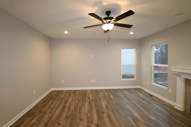 spare room with ceiling fan, dark wood-type flooring, and a tiled fireplace