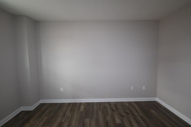 spare room featuring dark wood-type flooring and baseboards