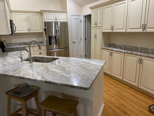 kitchen with a textured ceiling, stainless steel fridge with ice dispenser, light wood-type flooring, sink, and a breakfast bar