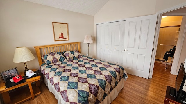 bedroom with a textured ceiling, light hardwood / wood-style flooring, a closet, and vaulted ceiling