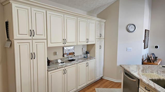 kitchen featuring stainless steel dishwasher, light wood-type flooring, cream cabinets, light stone counters, and a textured ceiling