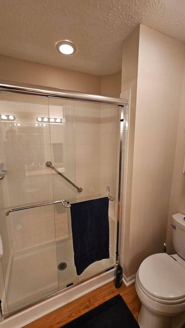 bathroom with toilet, a textured ceiling, a shower with door, and wood-type flooring