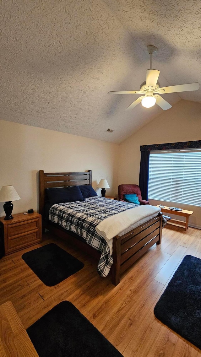 bedroom featuring ceiling fan, light hardwood / wood-style floors, a textured ceiling, and lofted ceiling