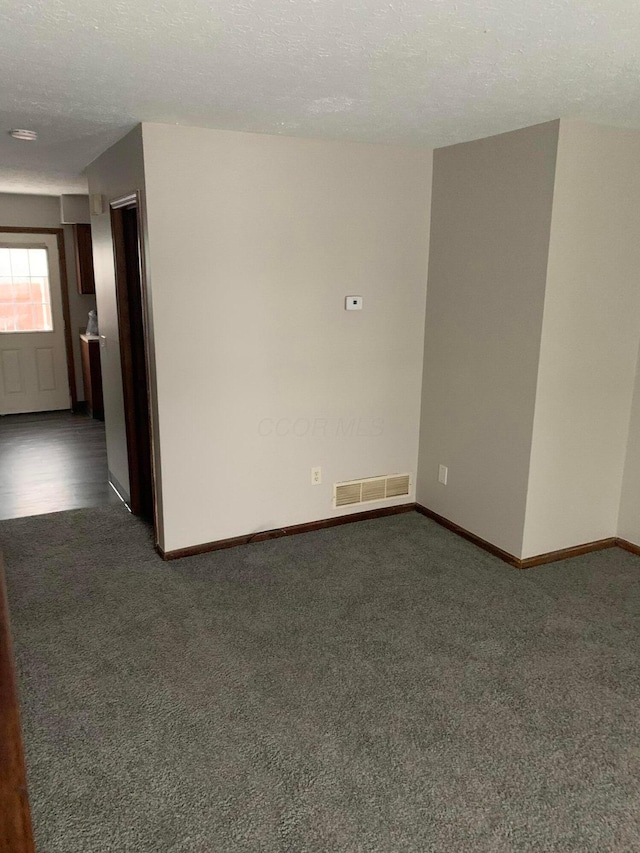 empty room with dark carpet and a textured ceiling