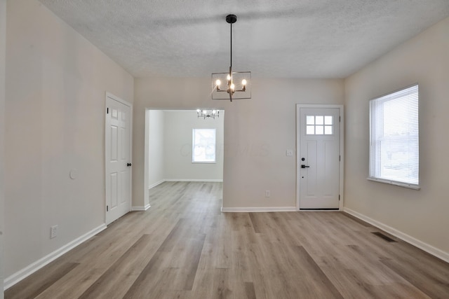 entrance foyer with an inviting chandelier, a textured ceiling, and light wood-type flooring