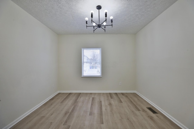 unfurnished room featuring an inviting chandelier, light hardwood / wood-style floors, and a textured ceiling