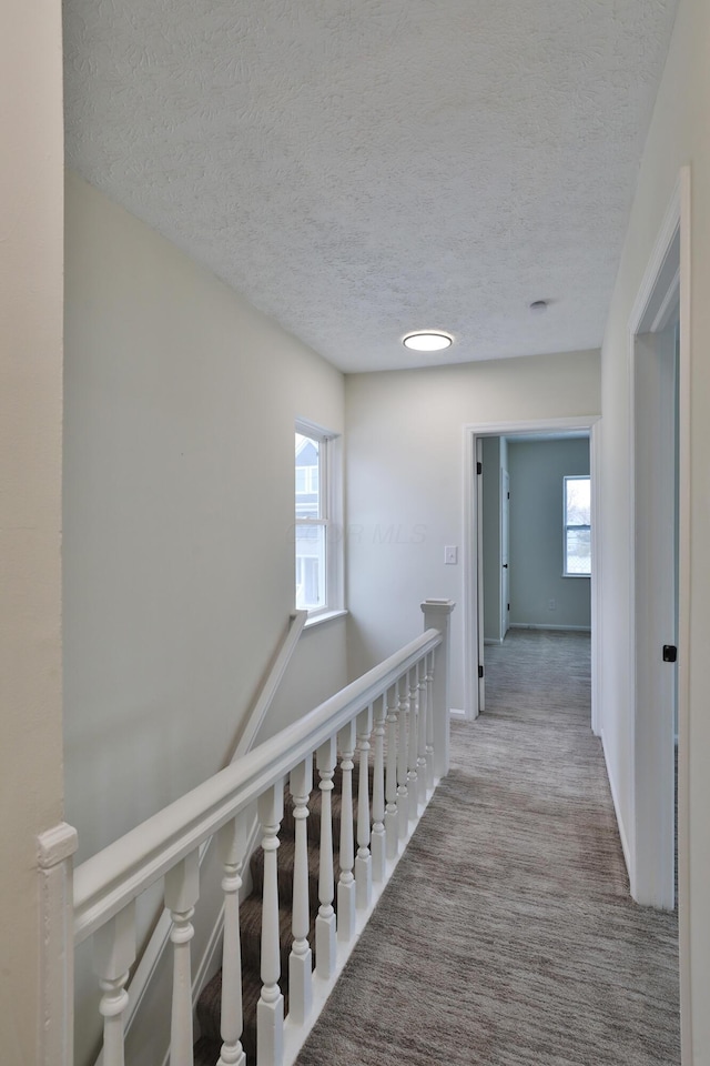 corridor with light colored carpet and a textured ceiling