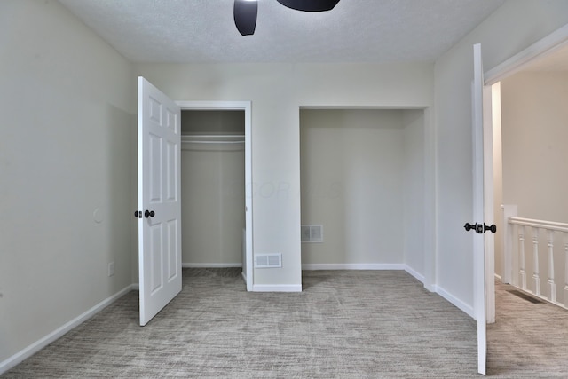 unfurnished bedroom featuring ceiling fan, light colored carpet, a closet, and a textured ceiling