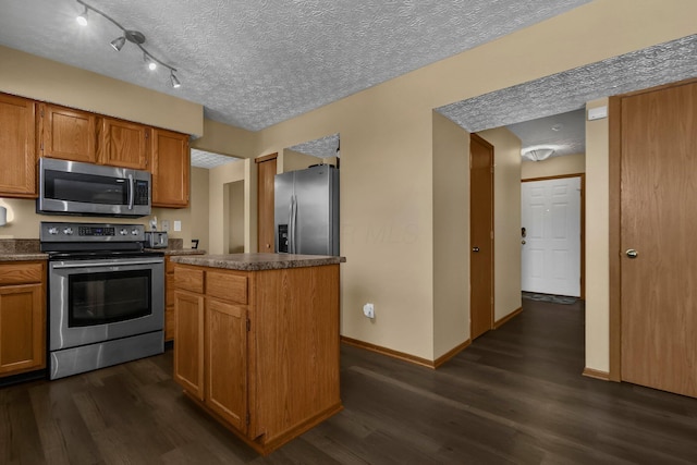 kitchen featuring appliances with stainless steel finishes, a textured ceiling, a kitchen island, and dark wood-type flooring