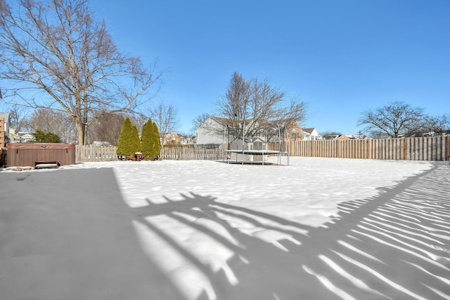 yard covered in snow featuring a trampoline and a hot tub