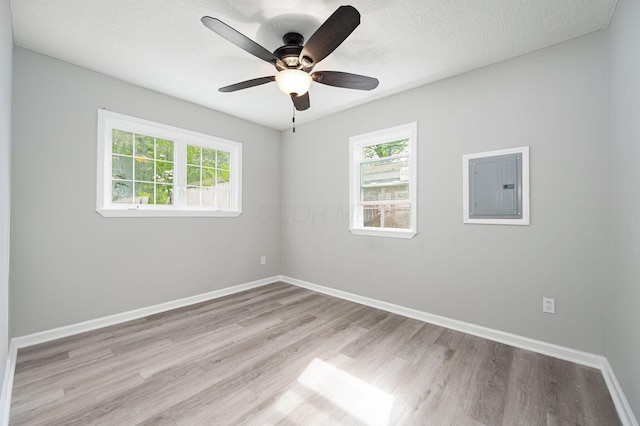 unfurnished room featuring light hardwood / wood-style floors, a textured ceiling, ceiling fan, and electric panel