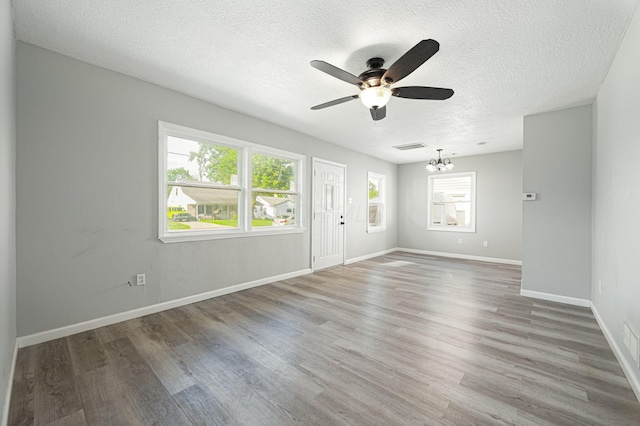 spare room featuring a textured ceiling, a wealth of natural light, ceiling fan with notable chandelier, and hardwood / wood-style flooring