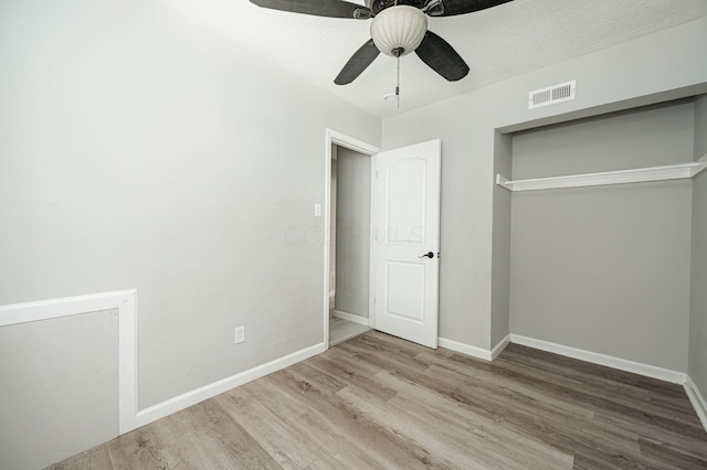 unfurnished bedroom with light wood-type flooring, a textured ceiling, ceiling fan, and a closet