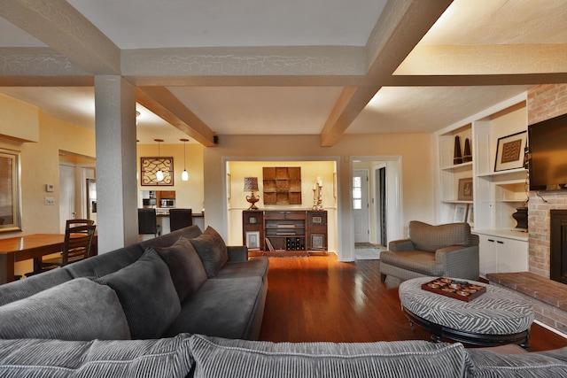 living room with beamed ceiling, wood-type flooring, a brick fireplace, and built in features