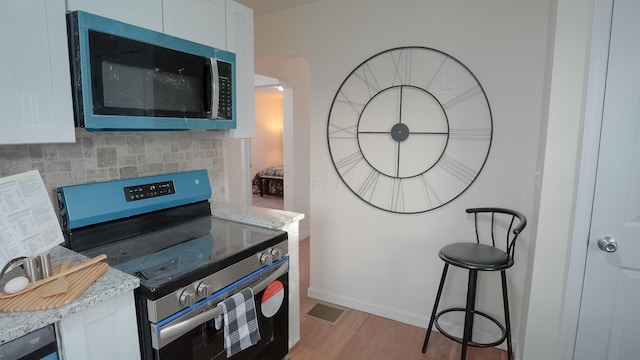 1807 Weiler Ave, Columbus, OH 43207 - kitchen with stainless steel appliances, white cabinets, light wood-type flooring, tasteful backsplash, and light stone countertops