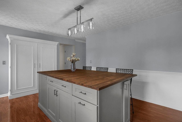 kitchen with hanging light fixtures, dark wood-type flooring, white cabinets, a center island, and butcher block counters