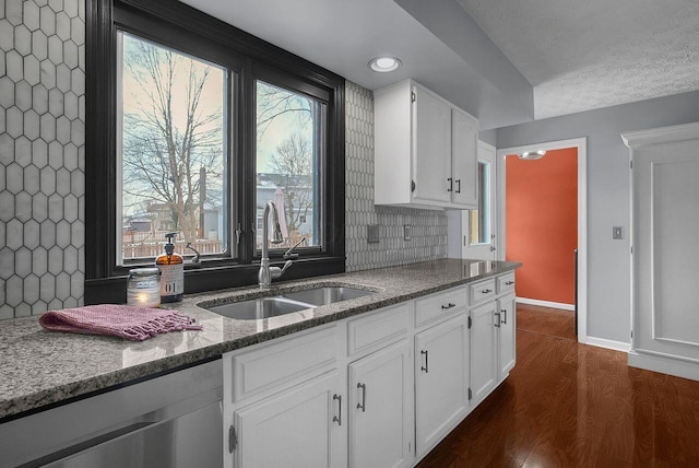 kitchen featuring stainless steel dishwasher, dark hardwood / wood-style flooring, sink, white cabinets, and stone counters