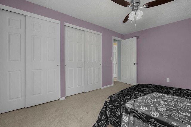 carpeted bedroom featuring multiple closets, ceiling fan, and a textured ceiling