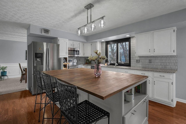 kitchen with white cabinetry, butcher block counters, a center island, and stainless steel appliances