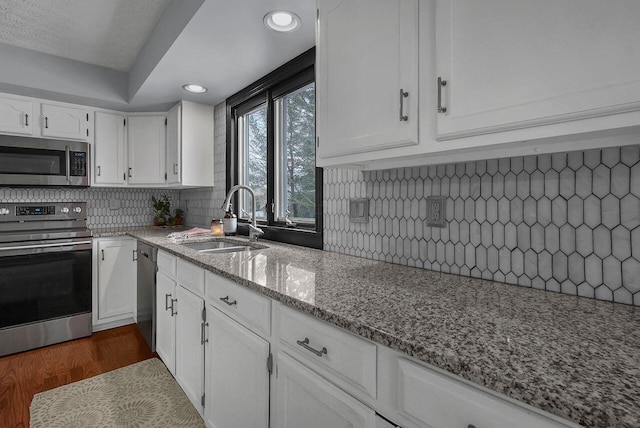 kitchen featuring appliances with stainless steel finishes, sink, white cabinets, light stone countertops, and dark hardwood / wood-style floors