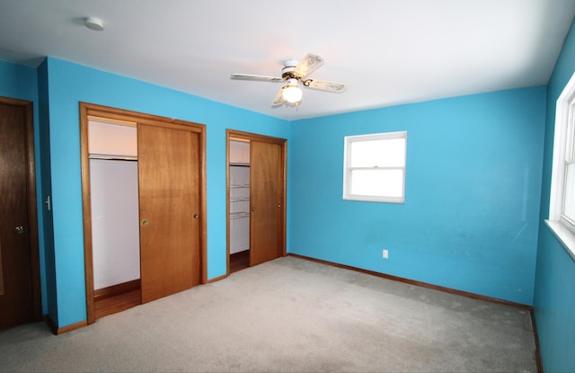 unfurnished bedroom featuring ceiling fan, multiple closets, and carpet flooring