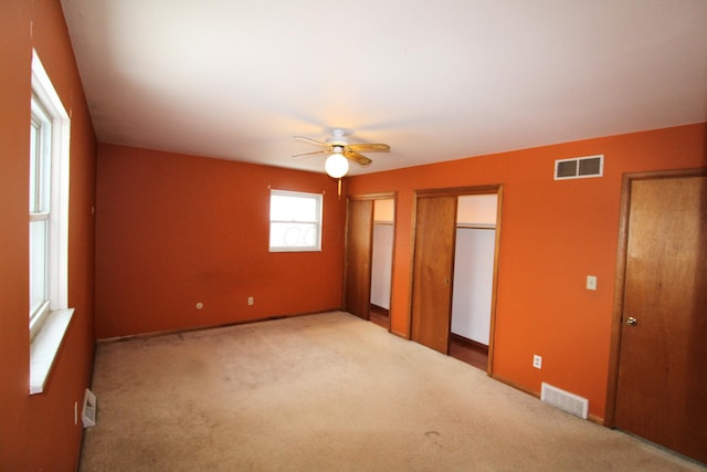 unfurnished bedroom featuring light carpet, ceiling fan, and multiple closets