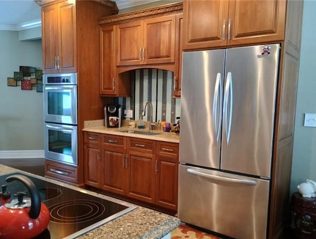 kitchen with brown cabinets, a sink, stainless steel appliances, crown molding, and baseboards