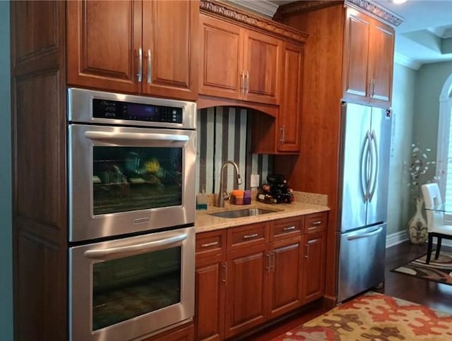 kitchen featuring light stone counters, wood finished floors, brown cabinetry, a sink, and appliances with stainless steel finishes