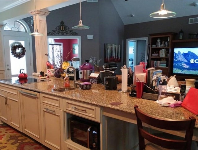 kitchen featuring visible vents, light stone counters, hanging light fixtures, ornate columns, and a sink