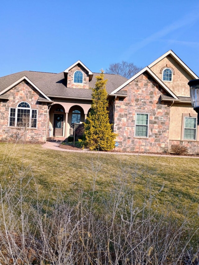 single story home with stucco siding, stone siding, roof with shingles, and a front yard