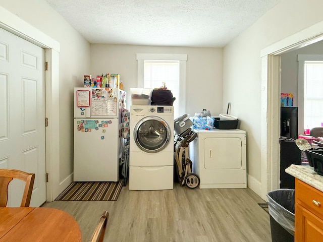 laundry room with light wood-type flooring, a textured ceiling, and washing machine and dryer