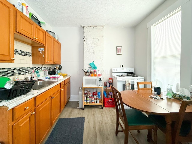 kitchen featuring white appliances, a textured ceiling, sink, backsplash, and light hardwood / wood-style flooring