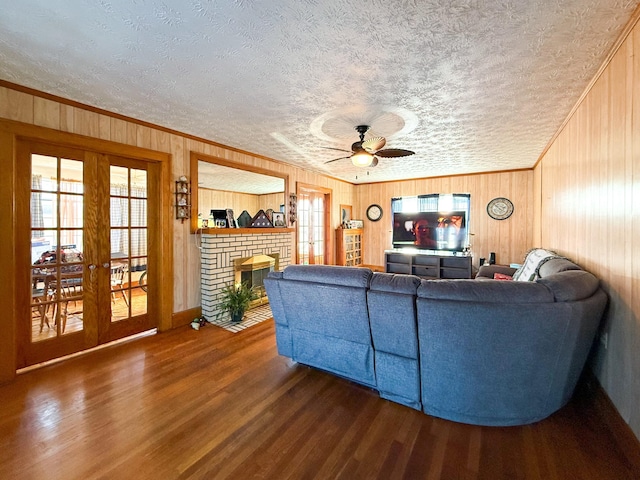 living room with ceiling fan, french doors, a brick fireplace, hardwood / wood-style floors, and a textured ceiling