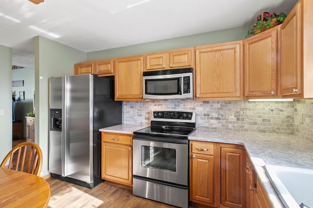 kitchen with light wood-type flooring, stainless steel appliances, tasteful backsplash, and sink