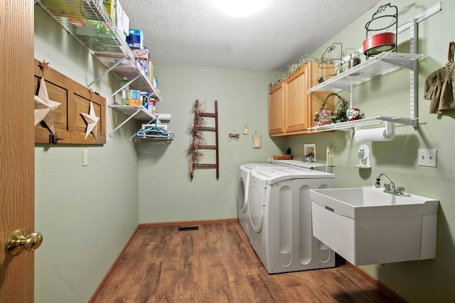 laundry area featuring dark hardwood / wood-style floors, sink, washer and clothes dryer, a textured ceiling, and cabinets