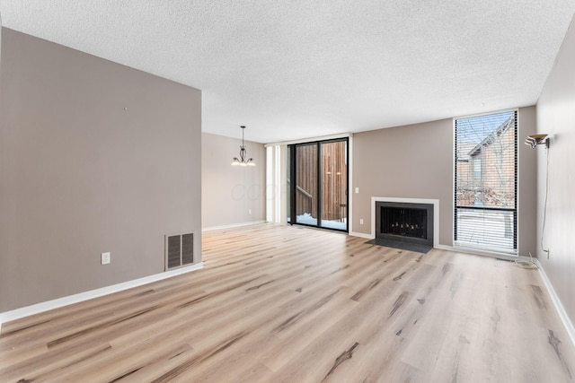 unfurnished living room featuring light hardwood / wood-style floors, a textured ceiling, and a notable chandelier