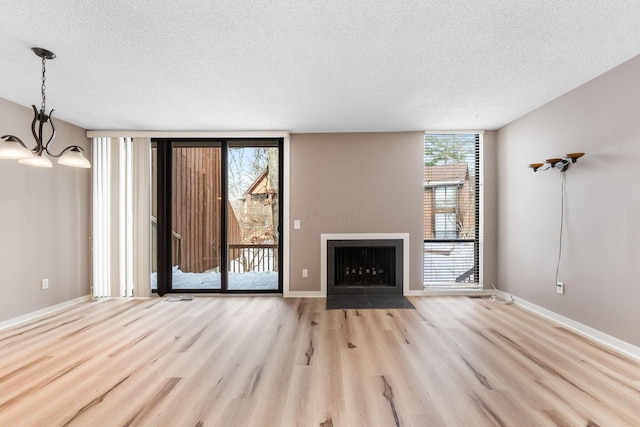 unfurnished living room featuring light wood-type flooring, an inviting chandelier, a textured ceiling, and expansive windows