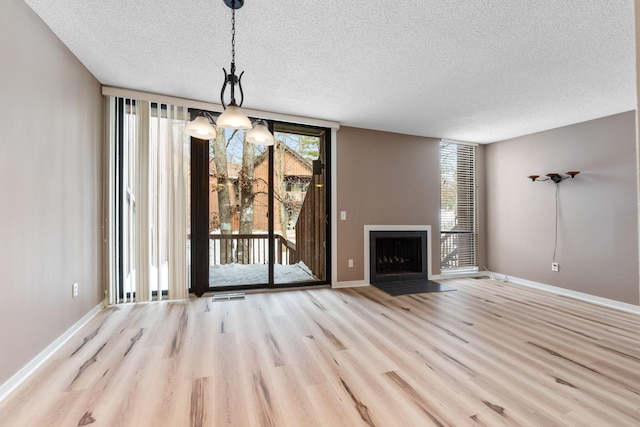 unfurnished living room featuring a textured ceiling, light hardwood / wood-style flooring, a notable chandelier, and expansive windows