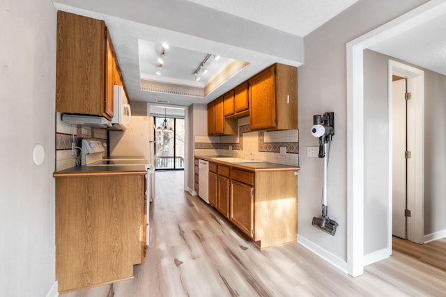 kitchen with white appliances, tasteful backsplash, sink, light wood-type flooring, and a tray ceiling