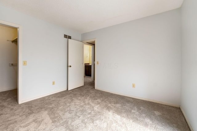 unfurnished bedroom featuring a spacious closet, light colored carpet, and a closet