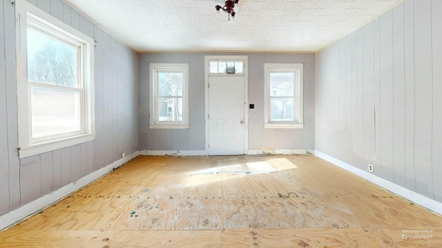 foyer featuring ornamental molding, a healthy amount of sunlight, and wood walls